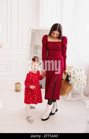 Mutter und kleine Tochter in roten Kleidern in einem hellen Schlafzimmer Stockfoto