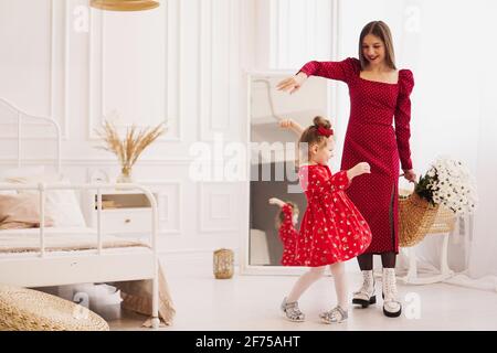 Mutter und kleine Tochter in roten Kleidern in einem hellen Schlafzimmer Stockfoto