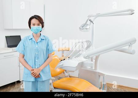 Junge asiatische Krankenschwester in medizinische Maske im Büro stehen Zahnklinik Stockfoto