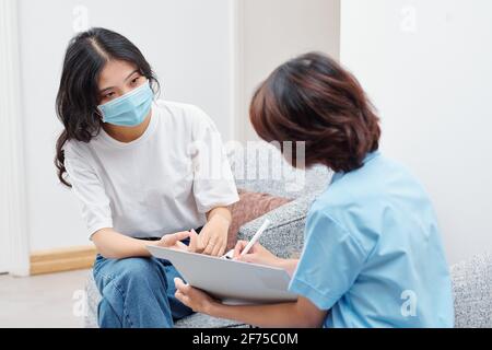 Krankenschwester, die Notizen im Dokument beim Gespräch mit Frau Patient in medizinischer Maske Stockfoto