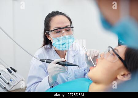 Reifer erfahrener Zahnarzt mit Brille und Schutzmaske, die Zähne bohrt Des Patienten, der an einer Kavität leidet Stockfoto