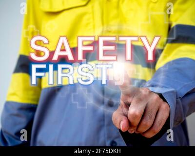 Arbeitsschutzkonzept. Das Wort „Safety First“ und das Hilfssymbol auf dem Zeigefinger von Technikern, die eine gelbe, gut sichtbare Jacke tragen. Stockfoto