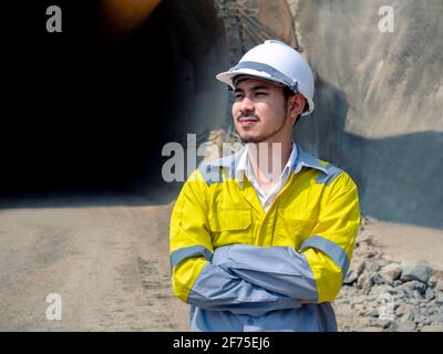 Porträt eines jungen hübschen asiatischen Tunnelbaus in gelber Höhe Visibility Jacke und weißer Schutzhelm stehen mit Armen gefaltet Vorne o Stockfoto