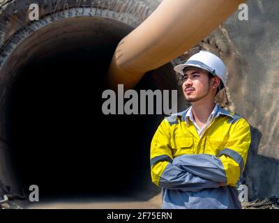 Porträt eines jungen asiatischen Tunnelbaus in gelber, gut sichtbarer Farbe Jacke und weißer Schutzhelm stehen mit eingeklappten Armen Vor dem rai Stockfoto