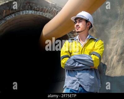 Porträt eines jungen asiatischen Tunnelbaus in gelber, gut sichtbarer Farbe Jacke und weißer Schutzhelm stehen mit eingeklappten Armen Vor dem rai Stockfoto