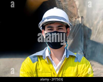 Portrait der jungen asiatischen Tunnelbau trägt eine gut sichtbare Jacke, Gesichtsmaske und weißen Schutzhelm stehen mit Armen vor der gefalteten Stockfoto