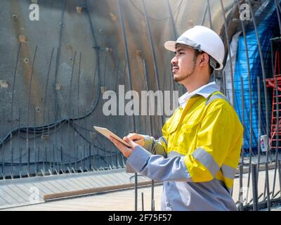 Junge schöne asiatische Tunnel Engineering trägt hohe Sichtbarkeit Jacke und Weißer Schutzhelm, der am Tunnel arbeitet und mit einem digitalen Tablet arbeitet Konstruktion Stockfoto