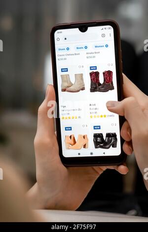 Frau liegt auf dem Sofa im Wohnzimmer und wählt ihre Schuhe über eine Online-Handy-App aus. Online-Shopping-Konzept. Vertikales Foto Stockfoto