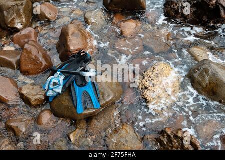 Während eines Urlaubs ruht eine Reihe blauer Masken, Schnorchel und Flossen auf Felsen am Ufer der Insel Stockfoto