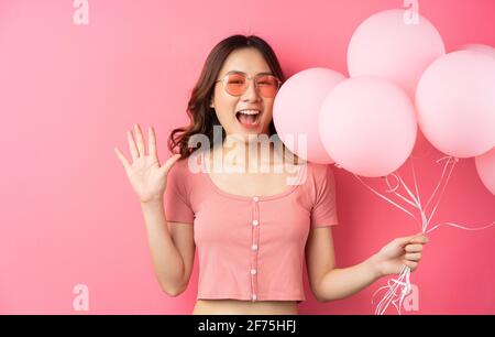 Die schöne Dame trägt eine Brille und hält Luftballons auf einem Rosa Hintergrund Stockfoto