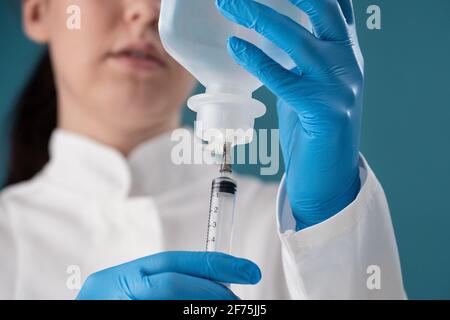 Eine junge Gesundheitsarbeiterin zieht eine Lösung aus einem Fläschchen zur Injektion in eine Spritze. Stockfoto