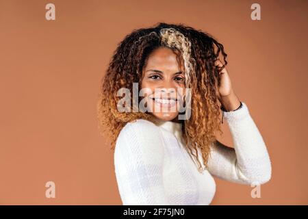 Erwachsene schwarze Frau mit lockigen Haaren lächelt im Studio vor braunem Hintergrund. Stockfoto
