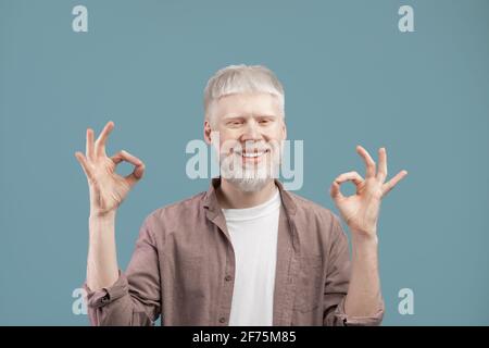 Glücklicher blonder Mann mit ungewöhnlichem Albino-Aussehen meditiert, seine Finger in Mudra, blauer Hintergrund Stockfoto