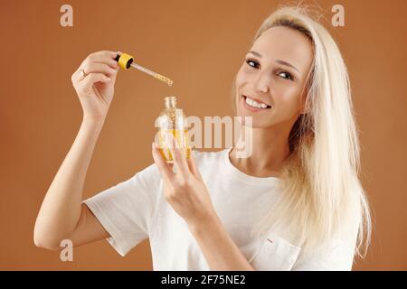 Porträt einer glücklichen jungen hübschen Frau mit einer Flasche Serum Oder Öl für Haar feuchtigkeitsspendend und Anlage Stockfoto