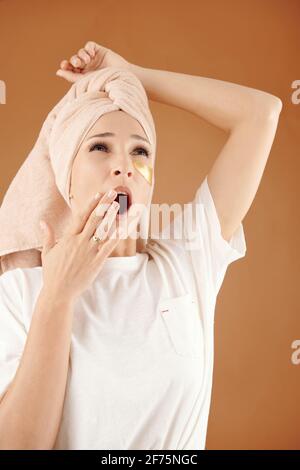Hübsche junge Frau mit einem Handtuch auf dem Kopf und einem verjüngenden Auge Gähnende Flecken Stockfoto