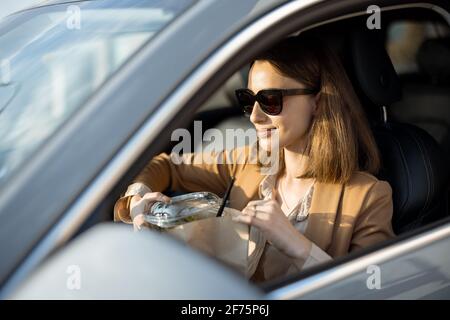 Schöne Frau, die im Auto einen heidnischen Salat isst. Ich habe eine Bestellung zum Essen erhalten. In der Mittagspause haben Sie einen schnellen Snack. Stockfoto