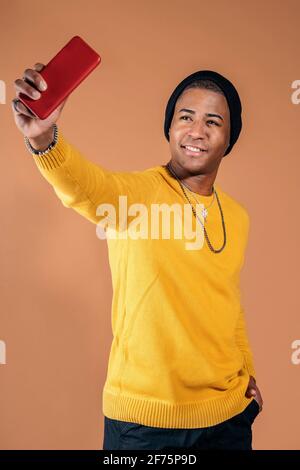 Junger Mann nimmt Selfie mit seinem Telefon im Studio vor braunem Hintergrund. Stockfoto