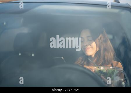 Schöne Frau, die im Auto einen heidnischen Salat isst und ein Telefon benutzt. Ich habe eine Bestellung zum Essen erhalten. In der Mittagspause haben Sie einen schnellen Snack. Stockfoto