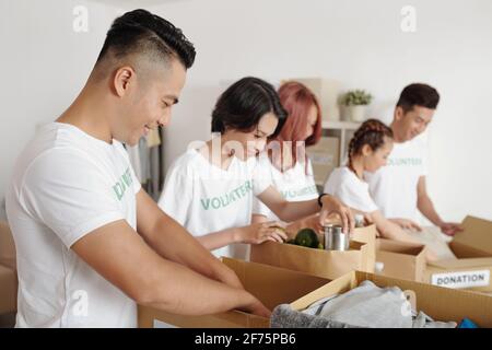 Gruppe junger asiatischer Freiwilliger, die Lebensmittel und Kleidung einpacken Pappkartons, um es Menschen in Not zu geben oder Flüchtlinge Stockfoto