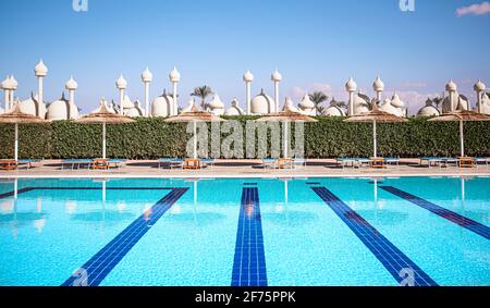 Strand mit Sonnenliegen, Strohschirme am Pool mit klarem Wasser. Resort in Ägypten. Stockfoto