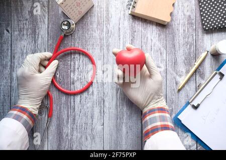 Arzt Hand hält rotes Herz und Stethoskop auf dem Tisch Stockfoto