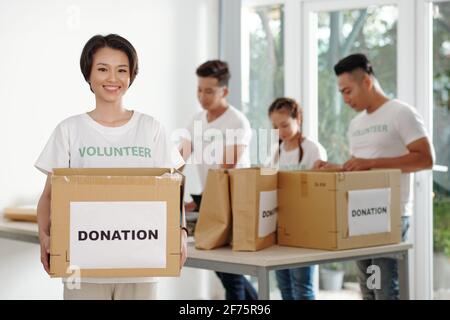Porträt einer glücklichen jungen vietnamesischen Frau mit großem Karton Arbeiten im Spendenzentrum Stockfoto