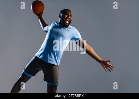 Junger afrikanischer Basketballspieler mit Basketball während des Spiels isoliert Grauer Hintergrund Stockfoto