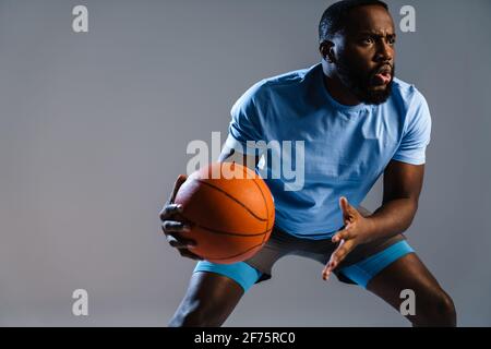 Junger afrikanischer Basketballspieler mit Basketball während des Spiels isoliert Grauer Hintergrund Stockfoto