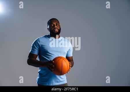 Junger afrikanischer Basketballspieler mit Basketball während des Spiels isoliert Grauer Hintergrund Stockfoto