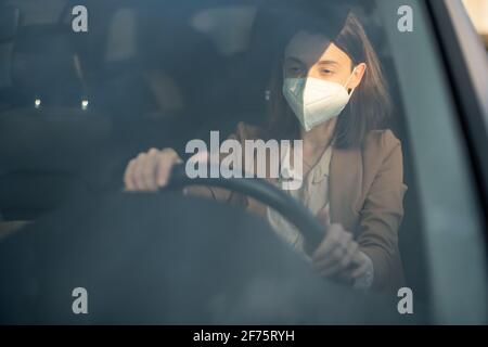 Junge Frau fährt Auto mit Schutzmaske auf ihrem Gesicht. Gesundheitswesen, Virenschutz, Allergieschutzkonzept. Stockfoto