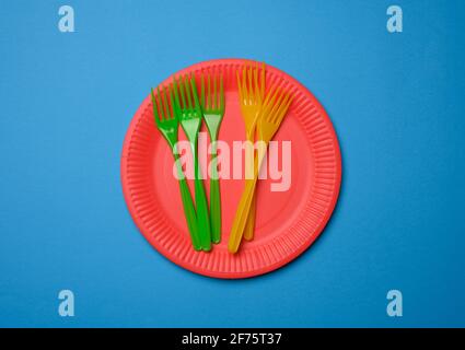 Grüne, orangefarbene Kunststoffgabeln und leere rote Papier-Einwegteller auf blauem Hintergrund, Set Stockfoto