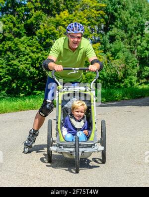 Mann eine skating Tour auf Inline Skates mit seinem kleinen Sohn im Buggy Stockfoto