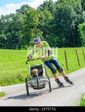 Mann eine skating Tour auf Inline Skates mit seinem kleinen Sohn im Buggy Stockfoto