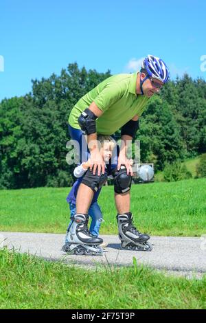 Mann eine skating Tour auf Inline Skates mit Hilfe seines kleinen Sohnes in der grünen Natur Stockfoto