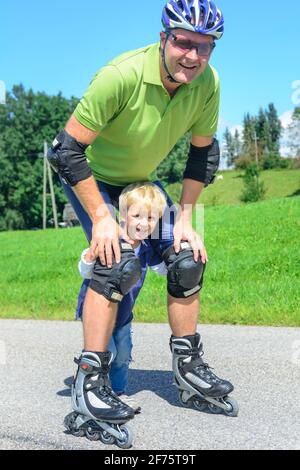 Mann eine skating Tour auf Inline Skates mit Hilfe seines kleinen Sohnes in der grünen Natur Stockfoto