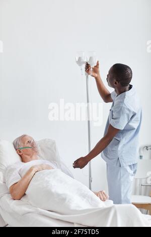 Vertikales Porträt eines afroamerikanischen Krankenpflegers, der IV-Tropf einführt Während der Behandlung des älteren Mannes im Krankenhausbett Stockfoto