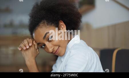 Fröhliche afroamerikanische Frau mit geballten Händen lächelnd und aussehend Bei der Kamera im Café Stockfoto