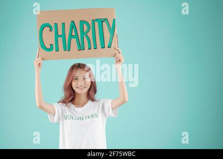 Lächelnd hübsche junge Freiwillige, die oben ein Charity-Papierschild hält Ihr Kopf Stockfoto