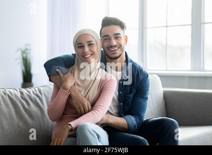 Liebendes arabisches Paar, das zu Hause auf der Couch sitzt und umarmt Stockfoto