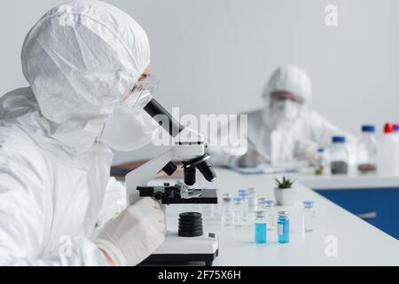 Wissenschaftler mit Mikroskop in der Nähe von Gefäßen mit Impfstoffen Stockfoto