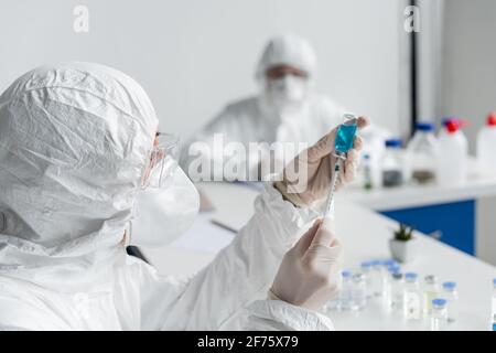 Wissenschaftler, der den Impfstoff in einer Spritze in der Nähe eines Kollegen auf verschwommen aufnahm Hintergrund Stockfoto