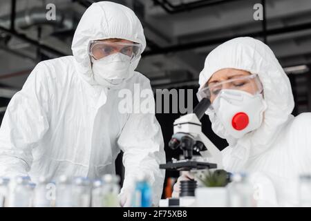 Wissenschaftler in der Nähe von Kollegen mit Mikroskop und Impfstoffen auf verschwommen Vordergrund Stockfoto