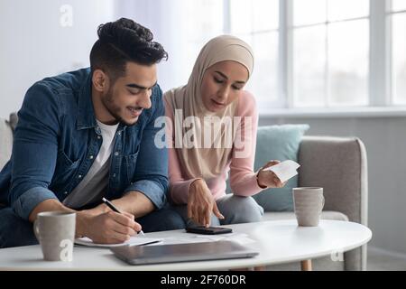 Positive muslimische Familie, die ihre Verauslagungen zählt, sich wohlhabend fühlt Stockfoto