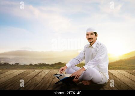 Asiatischer muslimischer Mann, der auf dem Koran sitzt und liest Holzfußboden Stockfoto