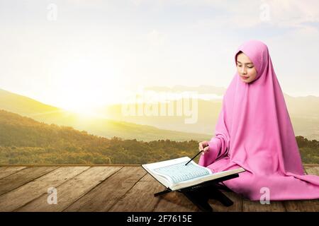 Asiatische muslimische Frau in einem Schleier sitzen und lesen die Quran auf dem Holzboden Stockfoto