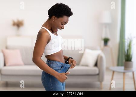 Aufgeregt Schlanke Afrikanische Frau Trägt Alte Übergroße Jeans Zu Hause Stockfoto