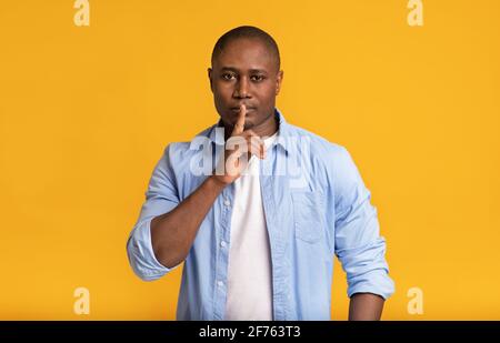 Serious zuversichtlich Geheimnis Erwachsene afroamerikanische Mann legt Finger auf Lippen und zeigt Zeichen der Stille Stockfoto