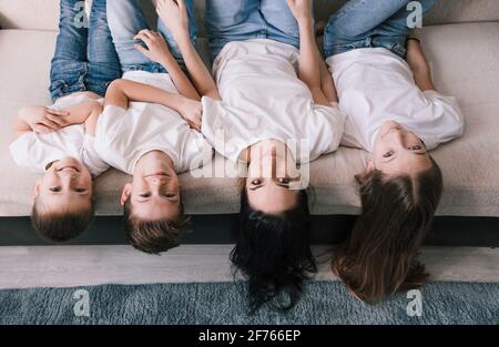 Meine Mutter, meine beste Freundin schöne lächelnde Brünette Mutter und Kinder senken ihren Kopf vom Sofa und schauen auf die Kamera. Stockfoto