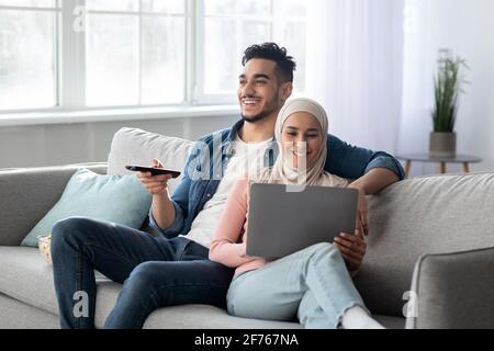 Glücklicher arabischer Mann mit ferngesteuerter Umarmung muslimischer Frau mit Laptop Stockfoto