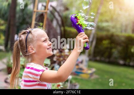 Portrait von niedlichen kleinen Bond-Kind Mädchen genießen Spaß Spielen Seifenblasen im Garten im Freien auf zu Hause Heller warmer Sommertag gegen Rasen Stockfoto